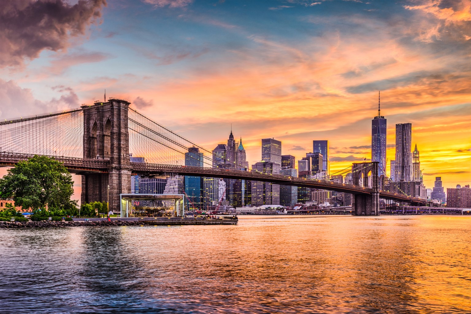 Brooklyn Bridge and New York City skyline at sunset with colorful sky reflecting over the East River