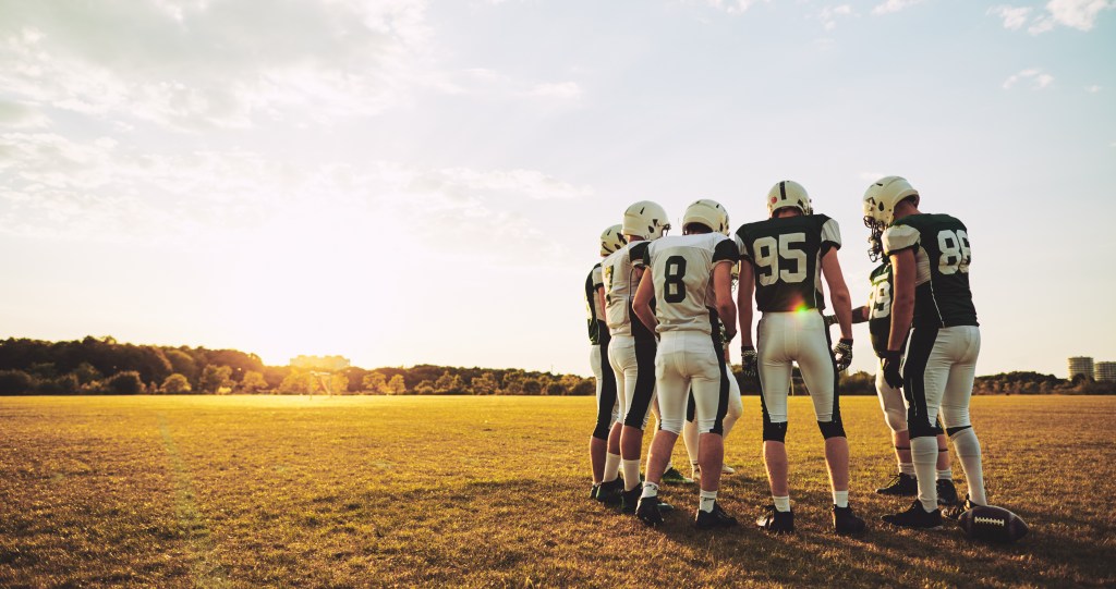 Group of young American football players standing in a circle talking strategy together during an afternoon practice