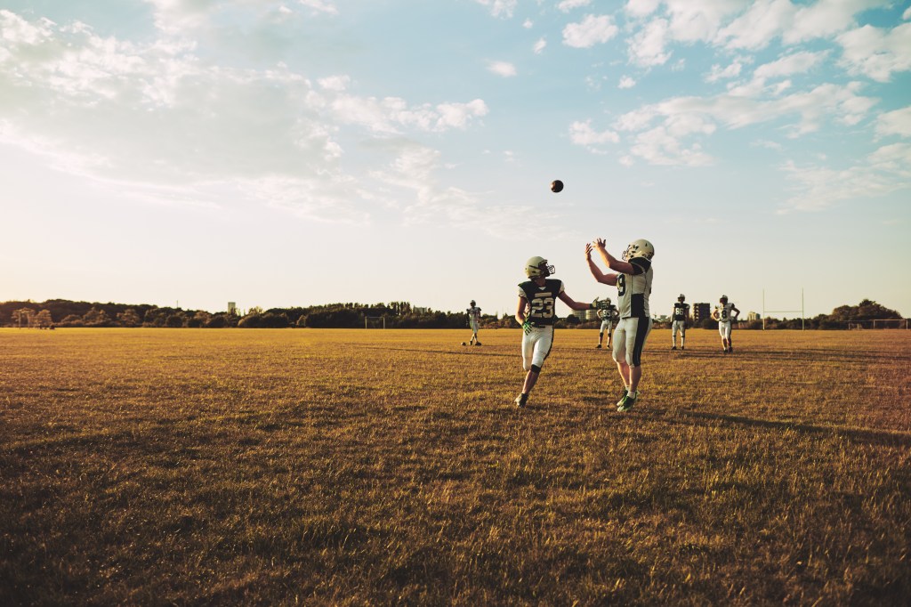 American football player running to catch a pass during team practice drills on a football field in the afternoon