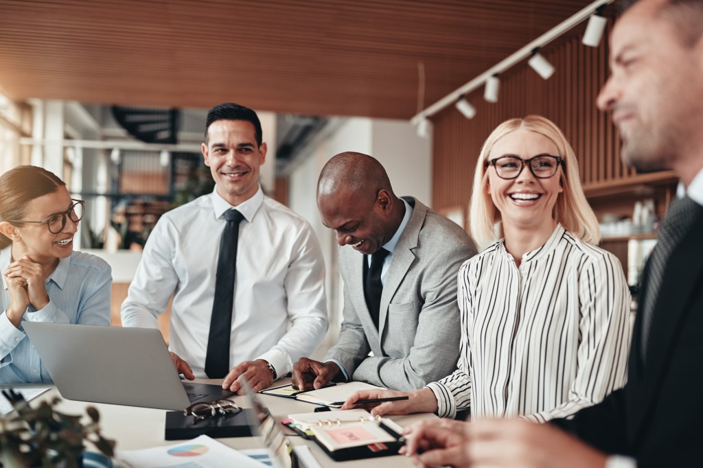 Group of diverse businesspeople laughing together during a meeting around a table in an office